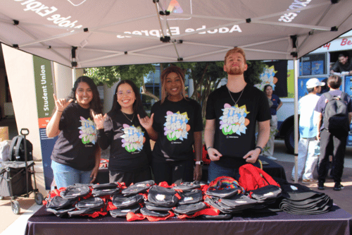group of students behind a table under a pop up tent giving out tote bags