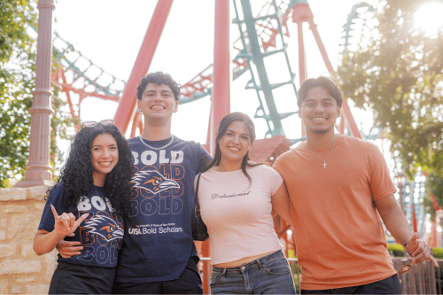 four students standing in front of a roller coaster