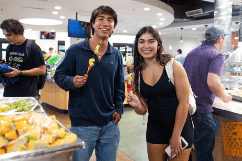 two students holding fruit skewers in Roadrunner Cafe