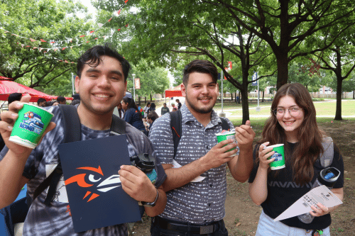 three students standing under a tree holding sno cones and bags