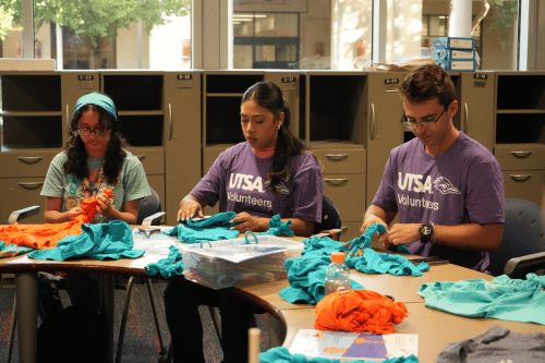 three students sitting at a table making dog toys from old fabric