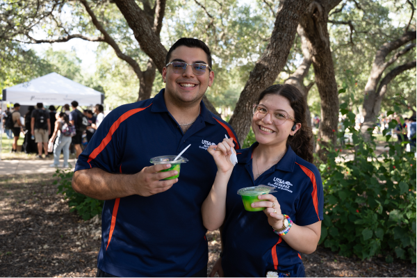 two student with raspas in hand standing in the shade of a tree