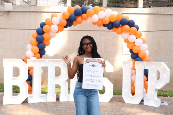a student poses in front of a balloon arch and large letters that say Birds Up