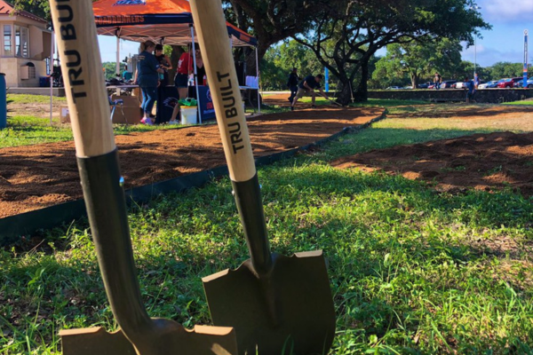 two shovels in the ground with two people standing near a tent in the background