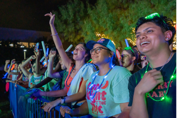 A group of students with glow accessories on watching the entertainment on stage