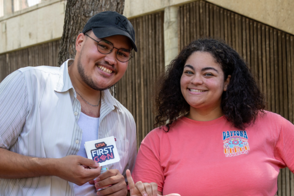 two students smiling and holding up First Gen stickers