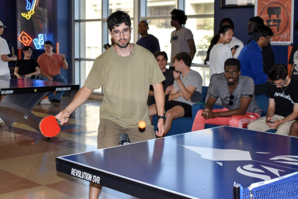 a male student playing ping pong while other students watch