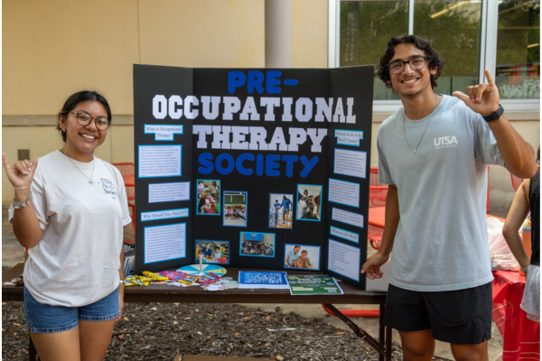 two students standing a table with a trifold with information about their student organization