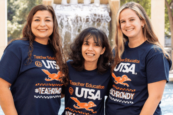 three students in teacher t-shirts in front of Sombrilla fountain